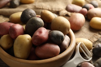 Photo of Different types of potatoes in bowl and peeler on table, closeup