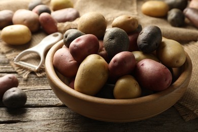 Photo of Different types of potatoes in bowl and peeler on wooden table, closeup