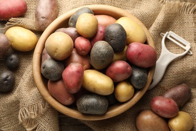 Photo of Different types of potatoes in bowl and peeler on table, flat lay
