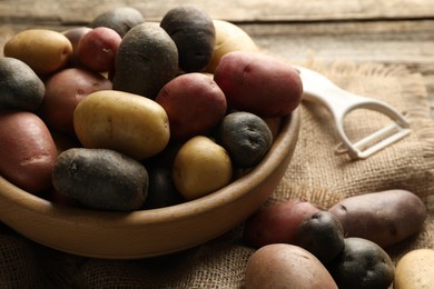Photo of Different types of potatoes in bowl and peeler on wooden table, closeup