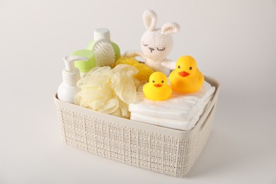 Photo of Baby accessories and body care products in basket on light grey background, closeup