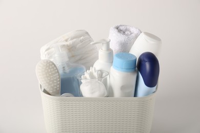 Photo of Baby accessories and body care products in basket on light grey background, closeup