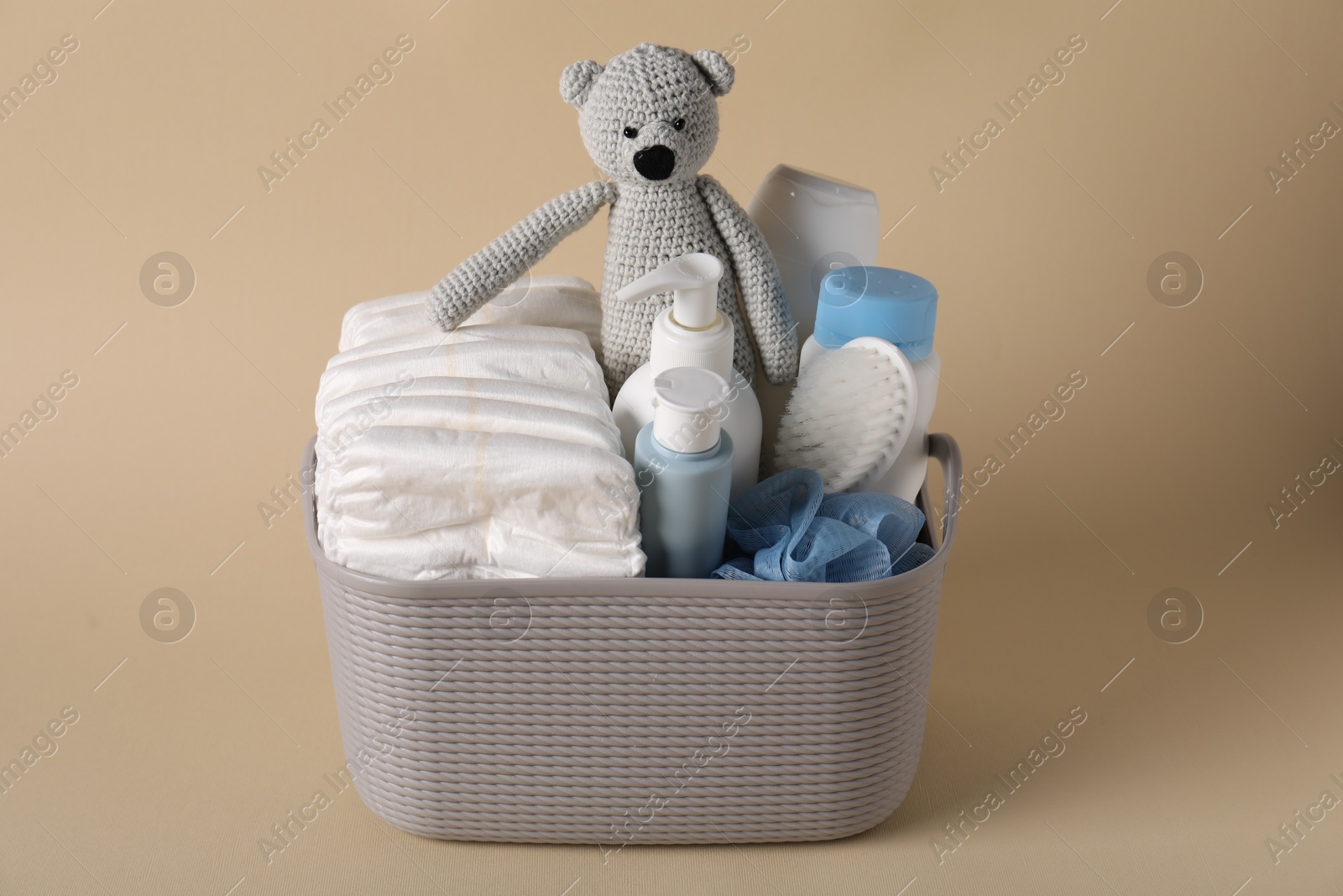 Photo of Baby accessories and body care products in basket on beige background