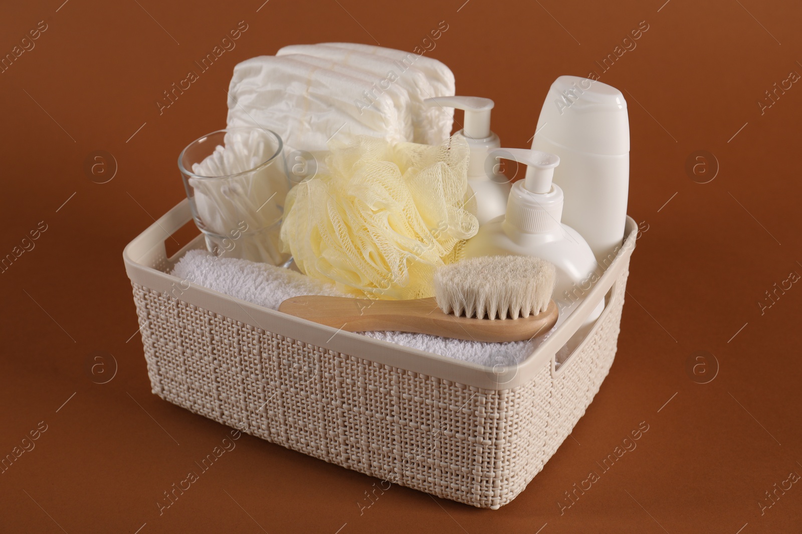 Photo of Baby accessories and body care products in basket on brown background, closeup