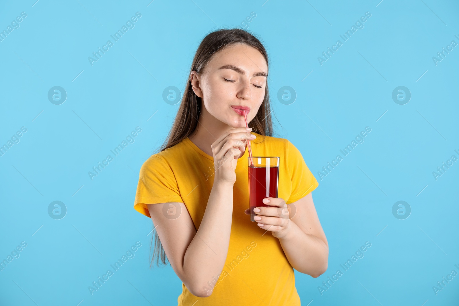 Photo of Woman drinking juice through straw on light blue background