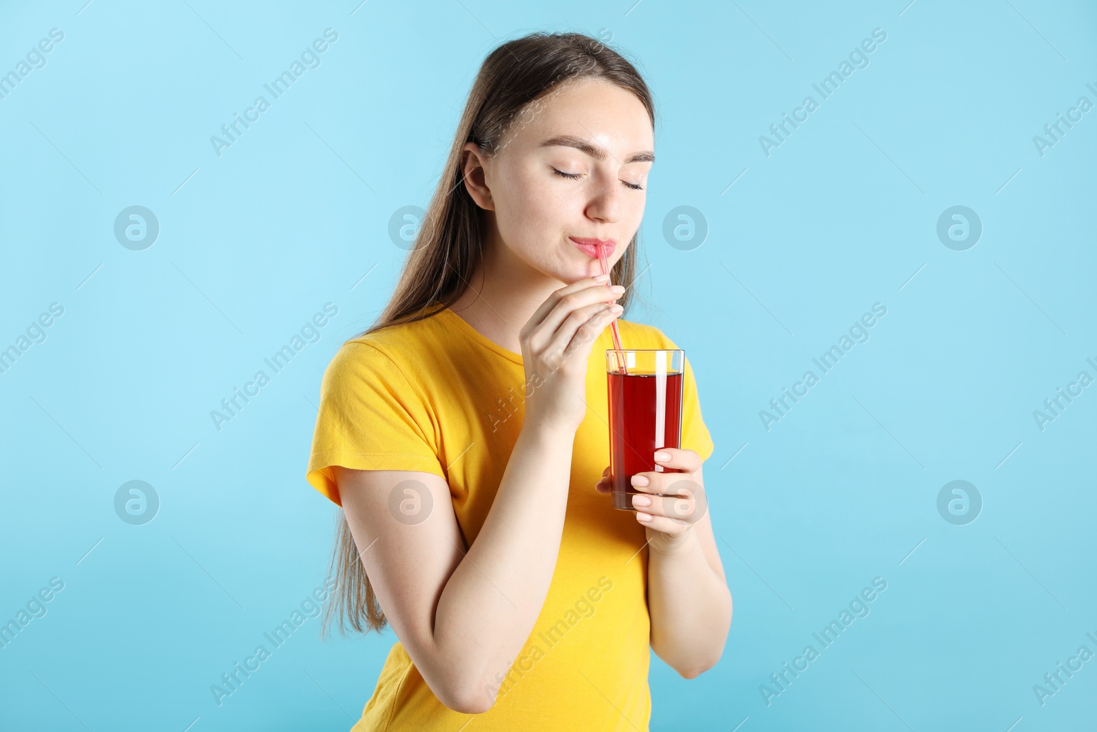 Woman drinking juice through straw on light blue background Photo of Woman drinking juice through straw on light blue background