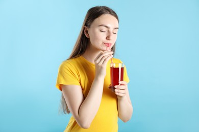 Photo of Woman drinking juice through straw on light blue background
