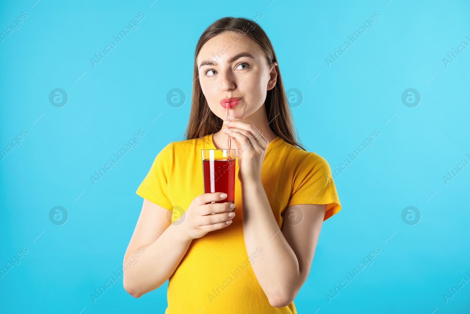 Photo of Woman drinking juice through straw on light blue background