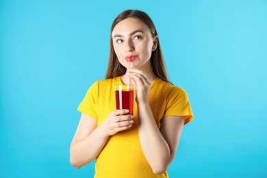 Photo of Woman drinking juice through straw on light blue background