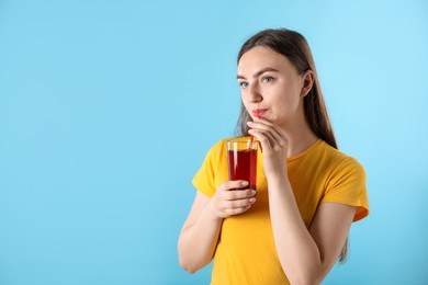 Photo of Woman drinking juice through straw on light blue background, space for text