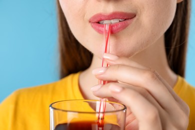 Photo of Woman drinking juice through straw on light blue background, closeup