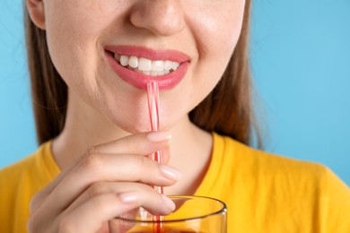 Photo of Woman drinking juice through straw on light blue background, closeup