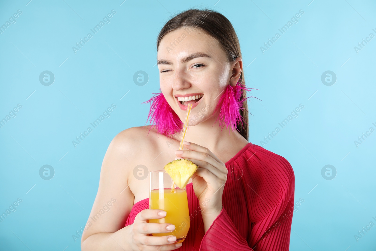 Photo of Woman drinking juice through straw on light blue background