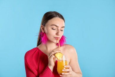 Photo of Woman drinking juice through straw on light blue background