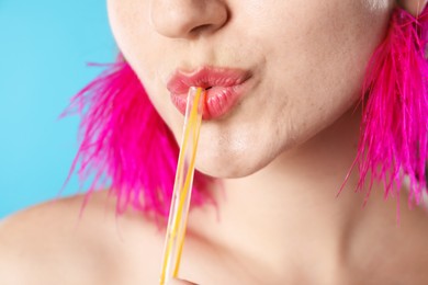 Photo of Woman drinking refreshing drink through straw on light blue background, closeup