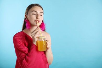 Photo of Woman drinking juice through straw on light blue background, space for text