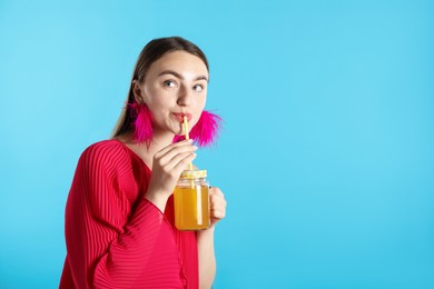Photo of Woman drinking juice through straw on light blue background, space for text