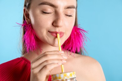Photo of Woman drinking refreshing drink through straw on light blue background