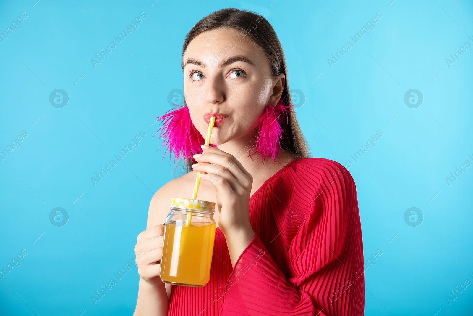 Woman drinking juice through straw on light blue background Photo of Woman drinking juice through straw on light blue background