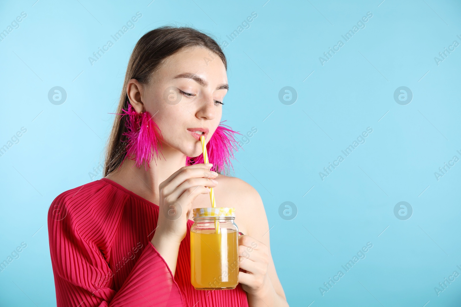 Photo of Woman drinking juice through straw on light blue background, space for text