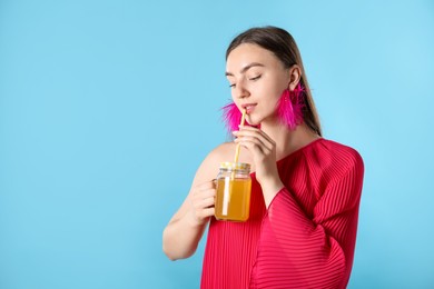 Photo of Woman drinking juice through straw on light blue background, space for text