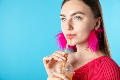 Photo of Woman drinking refreshing drink through straw on light blue background, space for text