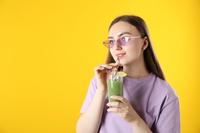 Photo of Woman drinking refreshing drink through straw on orange background, space for text
