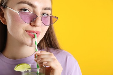 Photo of Woman drinking refreshing drink through straw on orange background, space for text