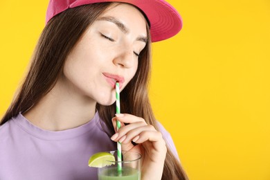 Photo of Woman drinking refreshing drink through straw on orange background, space for text