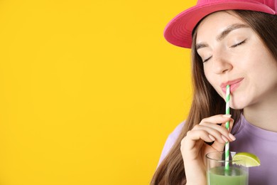 Photo of Woman drinking refreshing drink through straw on orange background, space for text
