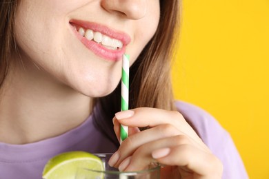Photo of Woman drinking refreshing drink through straw on orange background, closeup