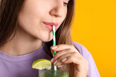 Photo of Woman drinking refreshing drink through straw on orange background, closeup