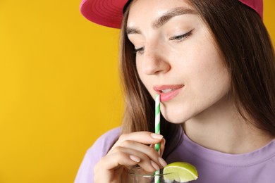 Photo of Woman drinking refreshing drink through straw on orange background, space for text
