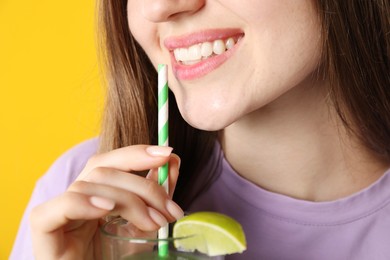 Photo of Woman drinking refreshing drink through straw on orange background, closeup