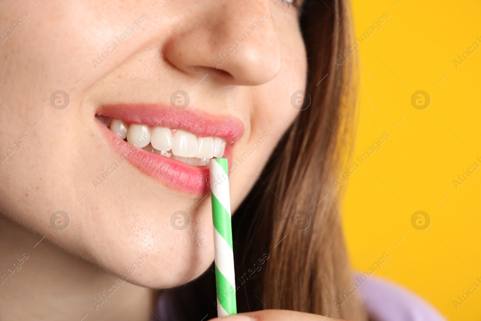 Photo of Woman drinking refreshing drink through straw on orange background, closeup
