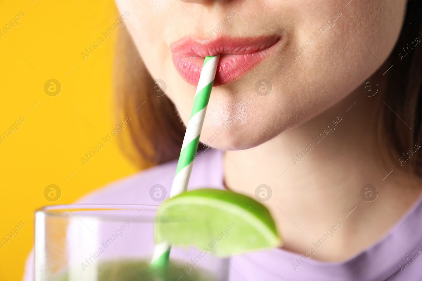 Photo of Woman drinking refreshing drink through straw on orange background, closeup