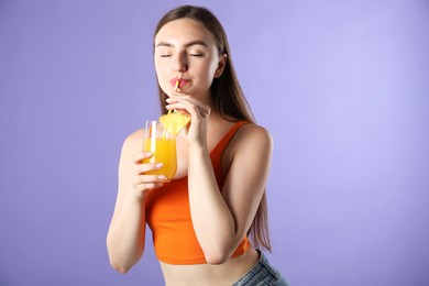 Photo of Woman drinking juice through straw on violet background