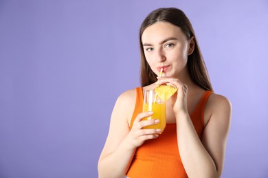Photo of Woman drinking refreshing drink through straw on violet background, space for text