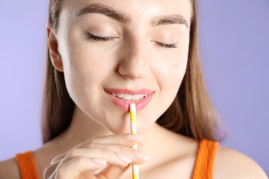 Photo of Woman drinking refreshing drink through straw on violet background