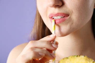 Photo of Woman drinking refreshing drink through straw on violet background, closeup
