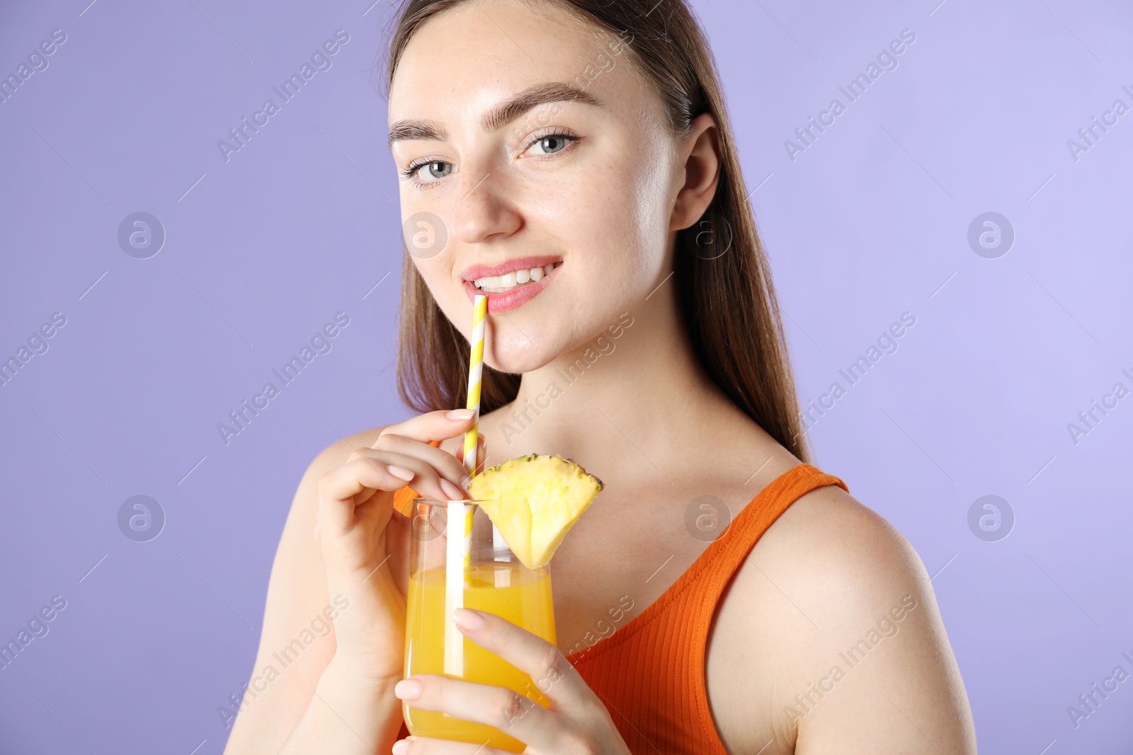 Photo of Woman drinking juice through straw on violet background