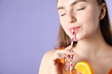 Photo of Woman drinking refreshing drink through straw on violet background, space for text