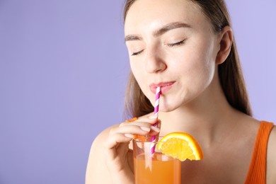 Photo of Woman drinking refreshing drink through straw on violet background, space for text