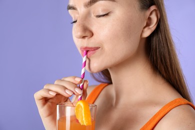 Photo of Woman drinking refreshing drink through straw on violet background, space for text