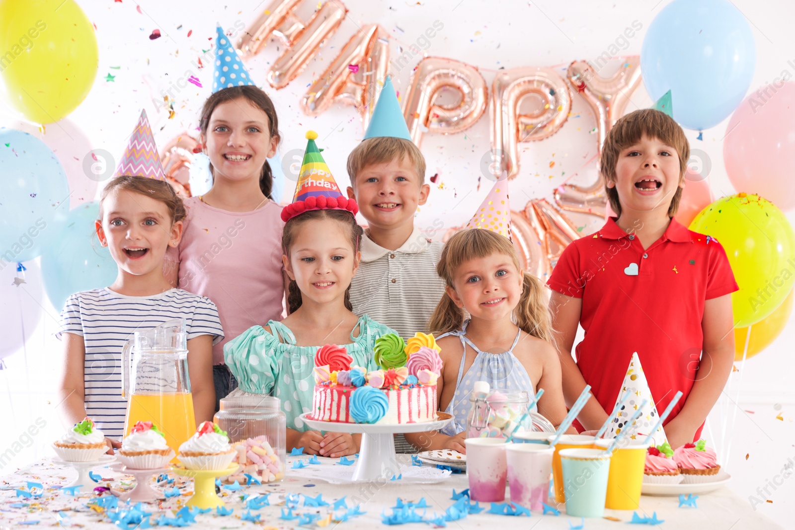 Birthday celebration. Kids at table with tasty cake and different treats in festive decorated room Photo of Birthday celebration. Kids at table with tasty cake and different treats in festive decorated room