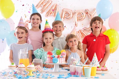 Photo of Birthday celebration. Kids at table with tasty cake and different treats in festive decorated room