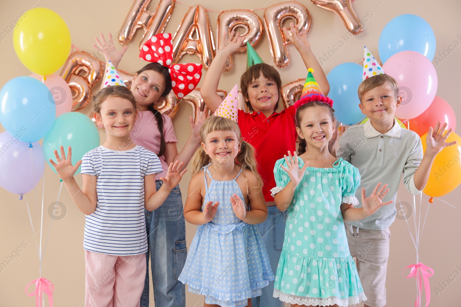 Birthday celebration. Happy kids with different festive decor on beige background Photo of Birthday celebration. Happy kids with different festive decor on beige background