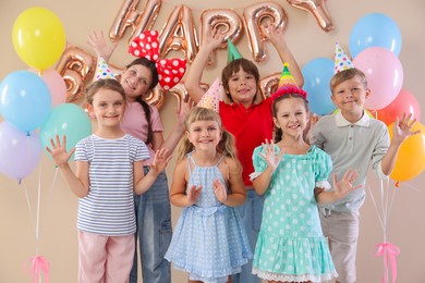 Photo of Birthday celebration. Happy kids with different festive decor on beige background