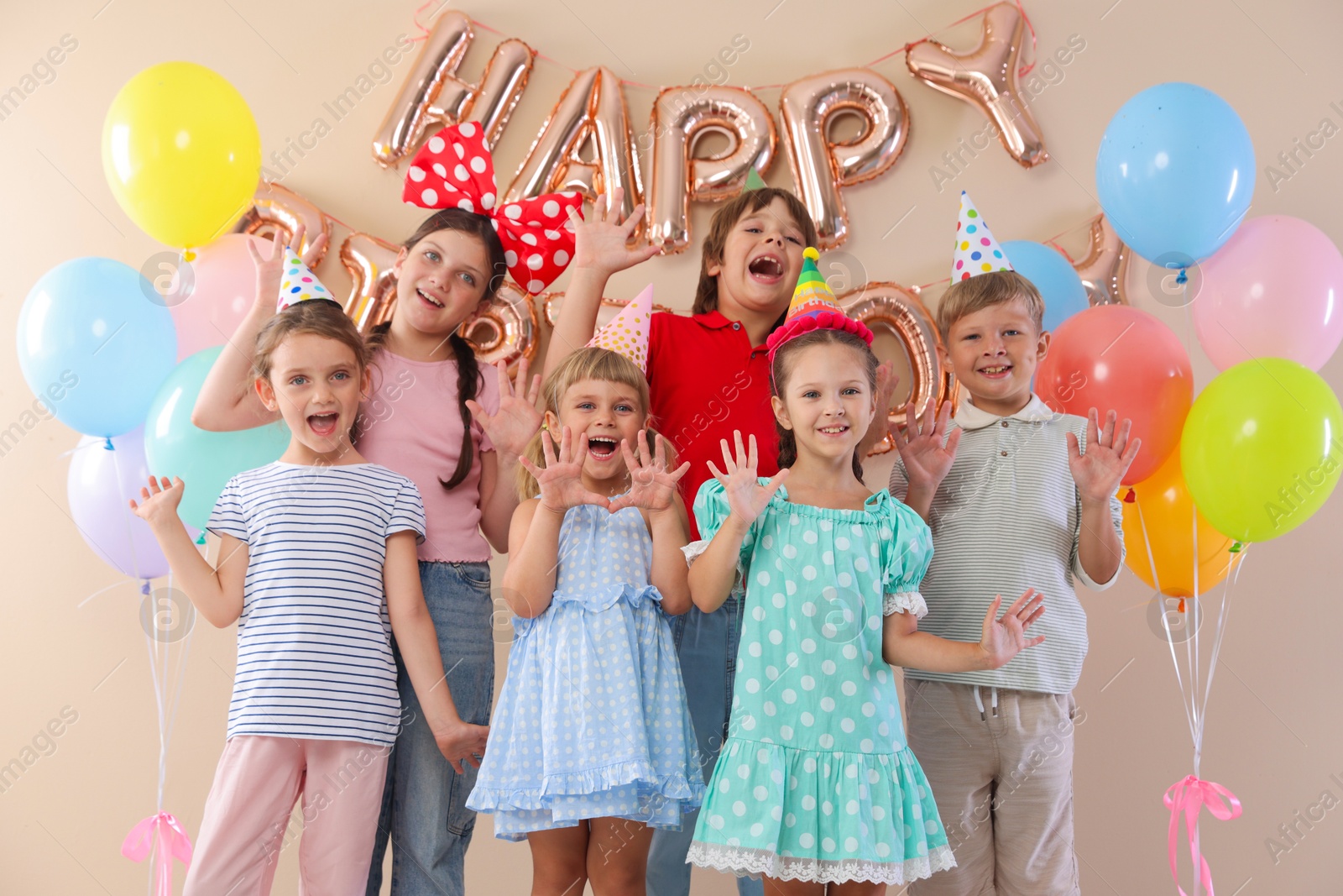 Birthday celebration. Happy kids with different festive decor on beige background Photo of Birthday celebration. Happy kids with different festive decor on beige background