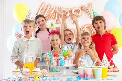 Photo of Birthday celebration. Kids at table with tasty cake and different treats in festive decorated room